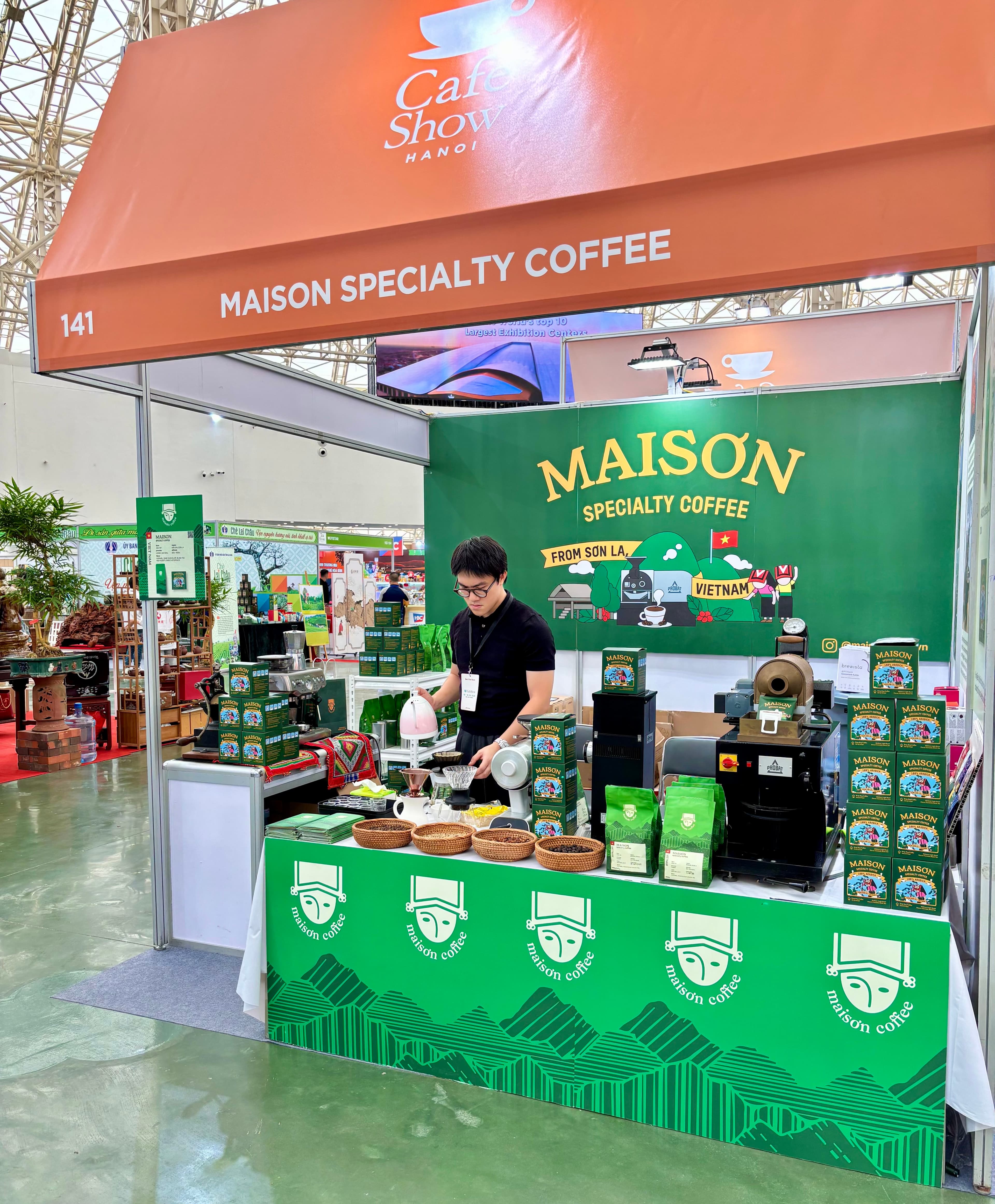 Gian hàng Maison Coffee tại Cafe Show Hà Nội, với các kệ cà phê Maison Specialty và nhân viên đang pha pour-over